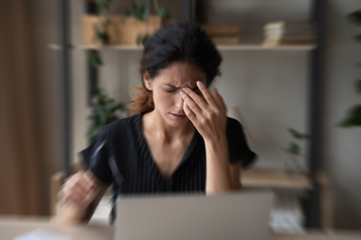 blurred image of woman with migraine holding head while sitting in front of laptop