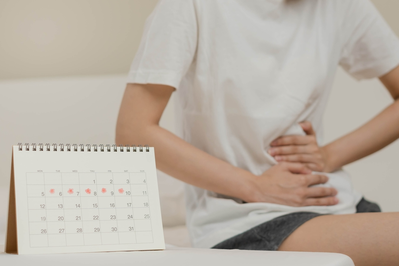 woman holding abdomen next to calendar marked with period dates