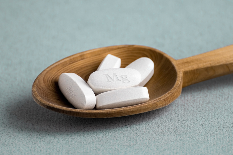 white pills labeled Mg in wooden spoon