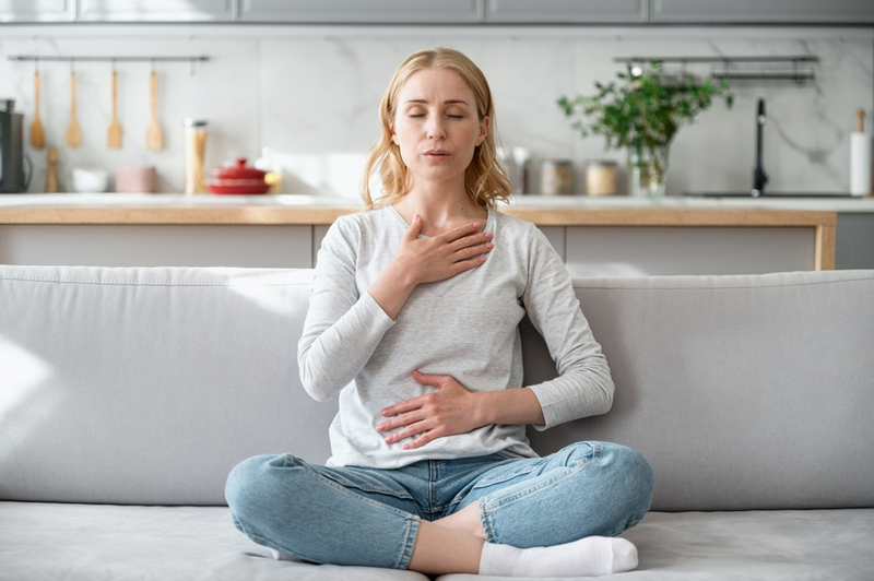 woman sitting on couch doing breathing exercises to calm anxiety symptoms