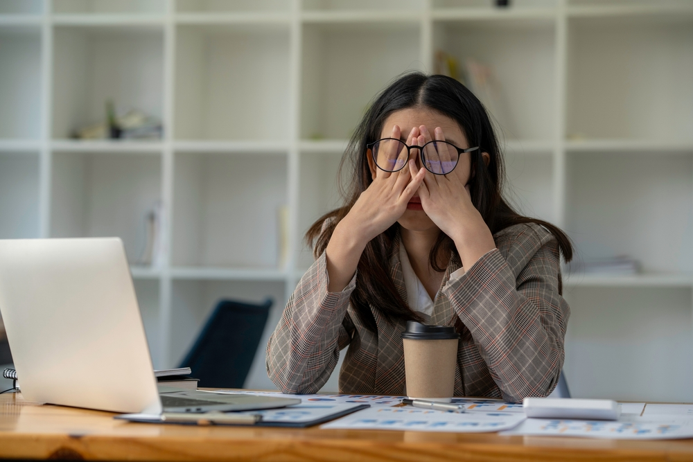 stressed businesswoman with head in her hands at work desk