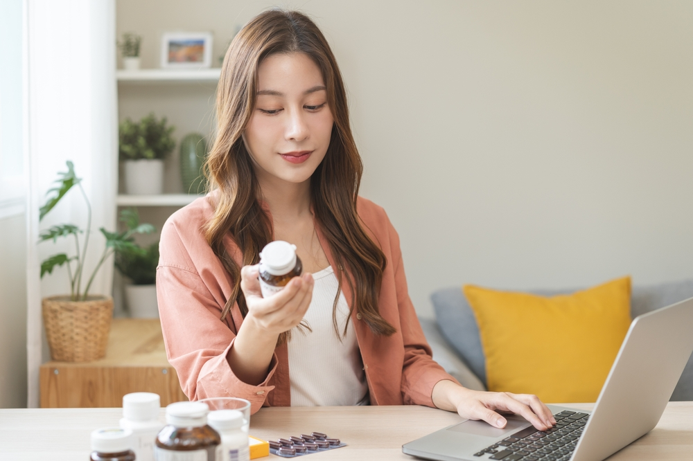 woman looking at supplement bottle label and researching ingredients on laptop
