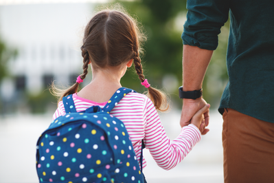 young girl wearing backpack and holding father's hand